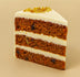 Slice of layered carrot cake with white frosting on a beige background  halo bagels harlem