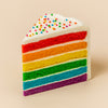 Slice of rainbow cake with white frosting and colorful sprinkles on a beige background  halo bagels harlem