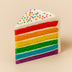 Slice of rainbow cake with white frosting and colorful sprinkles on a beige background  halo bagels harlem